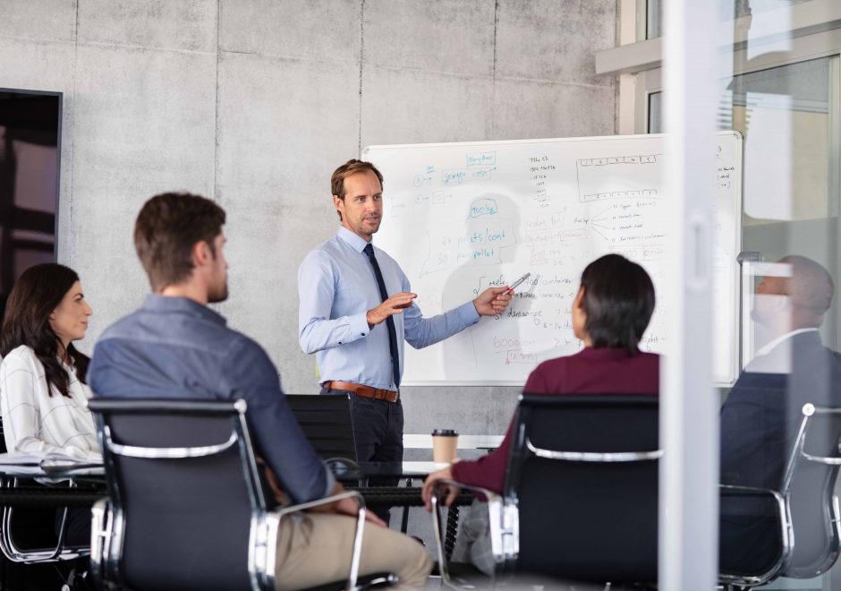 Mature businessman giving presentation to his colleagues in modern office. Leader presenting new project to business partners in conference room using white board. Businessman in a meeting talking.; Shutterstock ID 1665468751; purchase_order: -; job: -; client: -; other: -